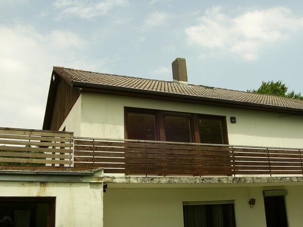 Wohnhaus vor der Sanierung: verwitterter Putz, alte Holzbrüstung am Balkon, altes Dach.